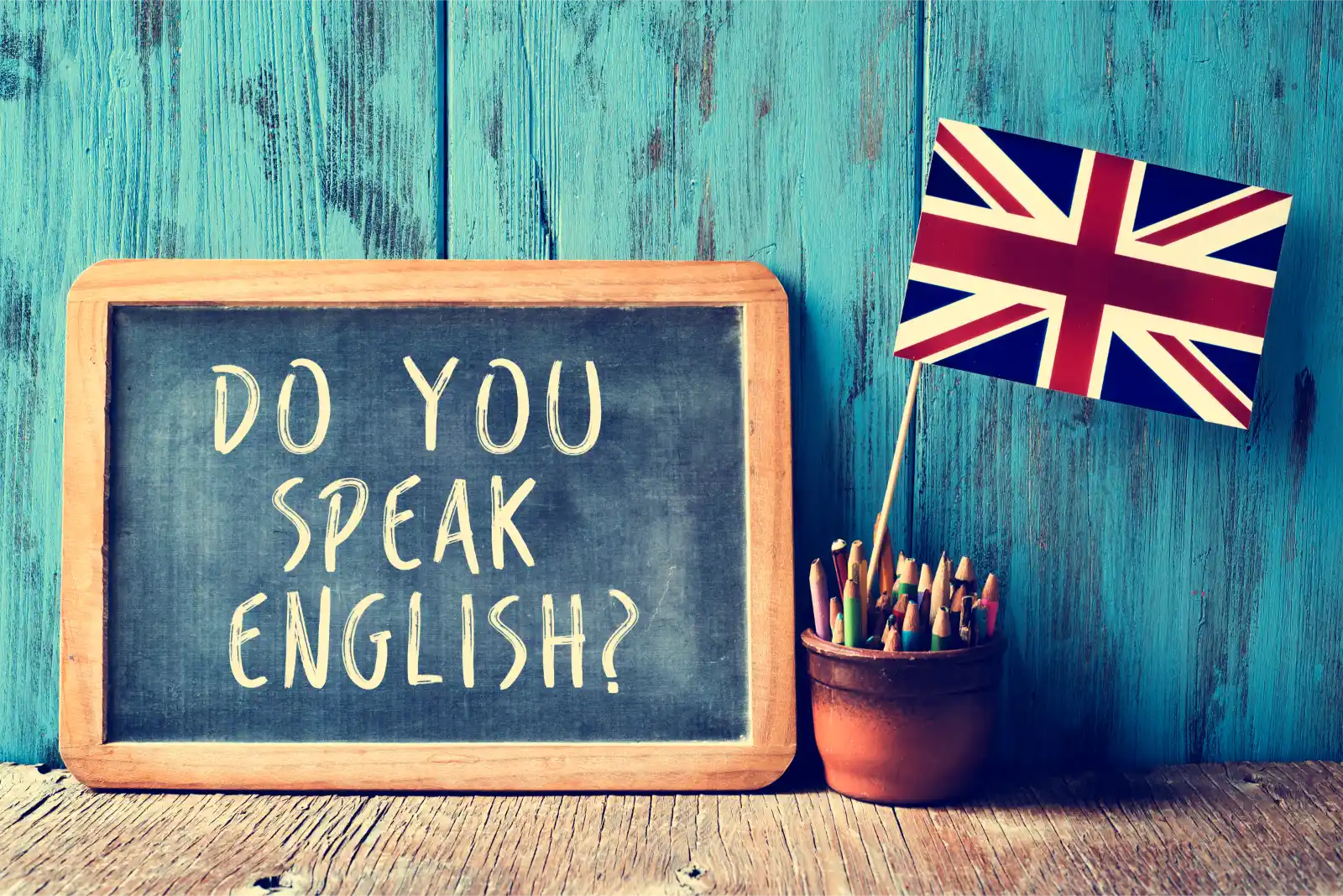 A blackboard with: 'Do you speak English?' written on it in white chalk, with a Union Jack next to it, so as to represent the English Language requirement for a UK visa.