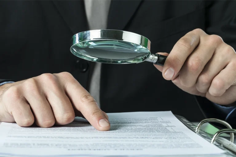 Man inspecting documents with a magnifying glass to carry out a Sponsor Licence check